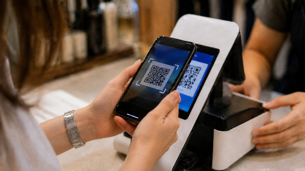 Person using a smartphone to scan a QR code at a contactless payment terminal